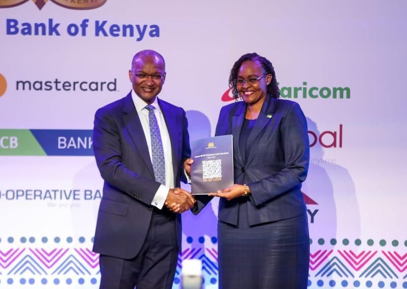 CBK Governor Dr. Patrick Njoroge hands over the Kenya Quick Response Code Standard Booklet to KCB Bank Kenya Managing Director Mrs. Annastacia Kimtai during the launch of the Kenya Quick Response Code Standard in Nairobi.